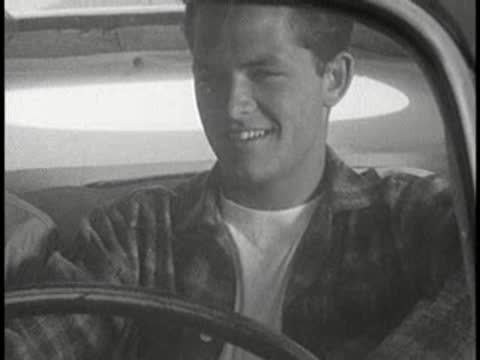 Driver smiling and laughing behind steering wheel in vintage car, 1960s