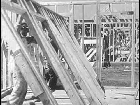 Construction workers raising wooden wall frames on a building site.
