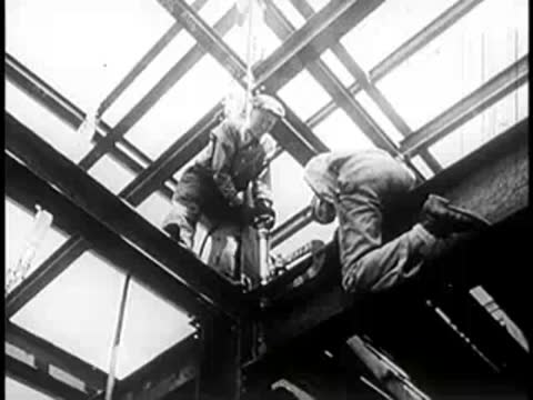Construction workers operating machinery on steel building framework.