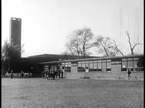 A modern school building exterior with a lawn and trees in front.