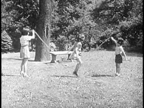 Children playing and jumping rope on a grassy park lawn.