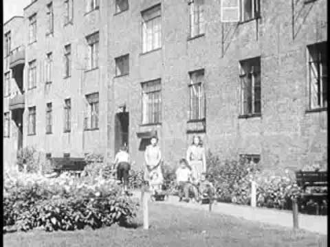 Apartment building exterior with a courtyard and people in the background.