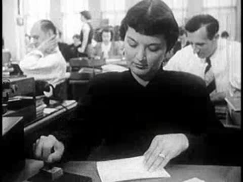 A woman sitting at a desk stamping documents in an office.