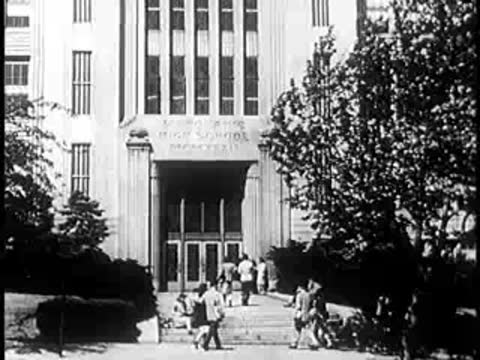 Exterior of a large civic building with trees and people on steps.