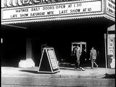 Movie theater marquee at night with signs and people outside.