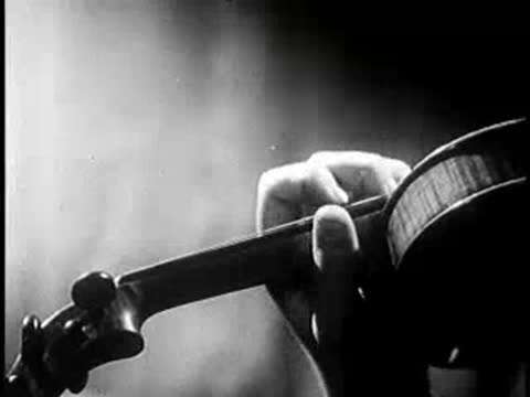 Close-up of fingers rapidly playing the strings of a violin in motion.
