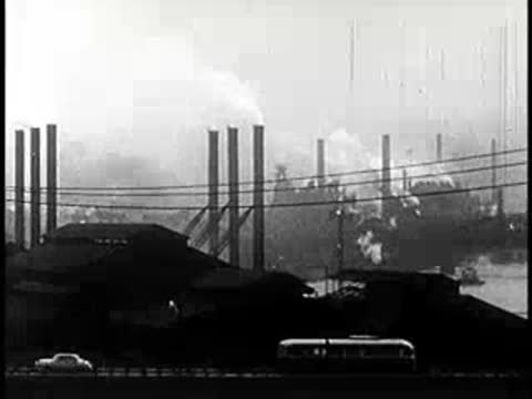 City skyline and industrial smokestacks emitting smoke along the water