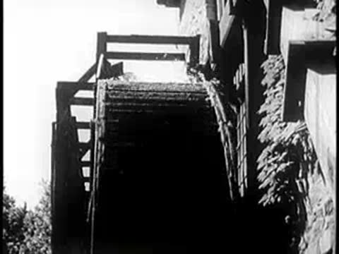 A water wheel turns continuously near a stone wall.