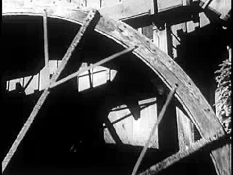 A large wooden water wheel rotates outdoors.