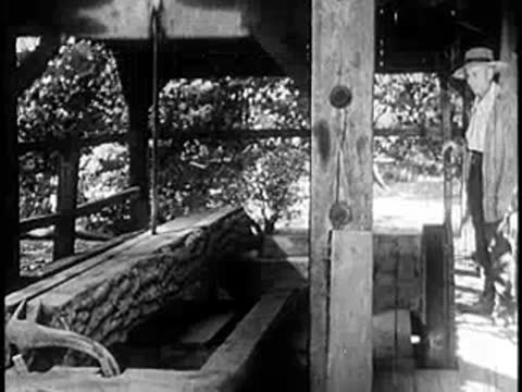 A man stands near a log on a sawmill machine.