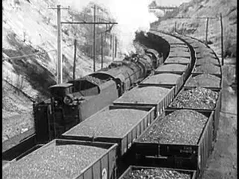 A steam train pulls a long line of cars along a curved track.
