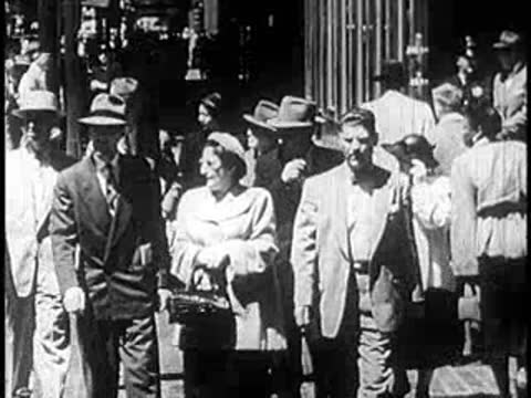 Pedestrians walking along a busy city sidewalk in the 1950s