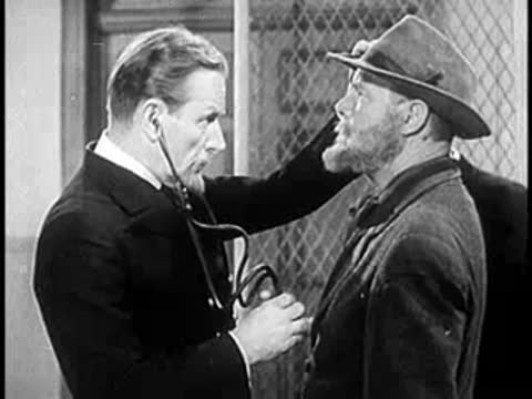 Doctor in dark suit listening to a man in a hat with a stethoscope