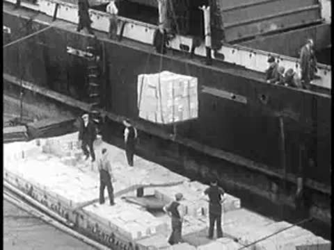 Workers loading heavy crates onto a barge from a dock side crane