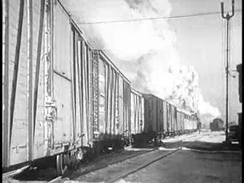 Freight train moving past a line of boxcars with steam and smoke
