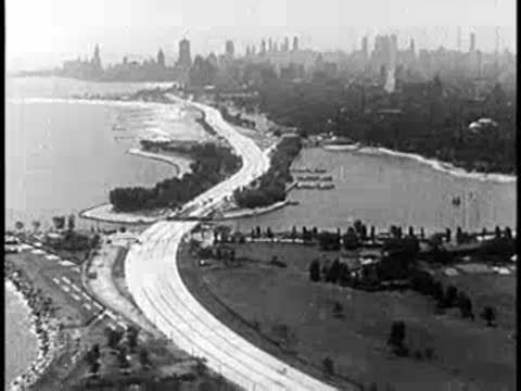 Aerial view of a coastal highway with city skyline in the background, 1940s style