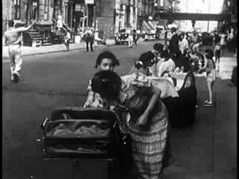 People strolling on a city sidewalk next to baby carriages, 1940s urban street life