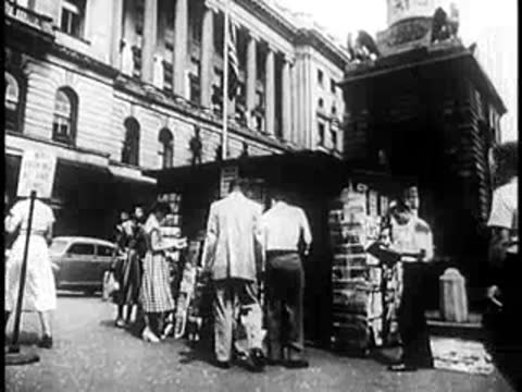 People gathered around an outdoor newspaper stand and kiosk on a city sidewalk