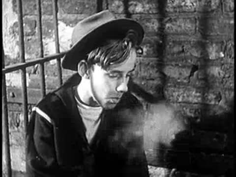 A young boy smoking a cigarette while leaning against a brick wall, close-up
