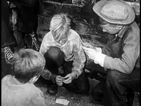 Two boys interacting on the ground while another person watches, alley scene