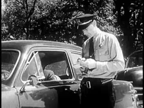 Police officer writing a ticket next to a parked car on a city street