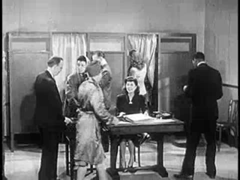 People interacting inside a busy office with privacy dividers and desks, 1940s workplace