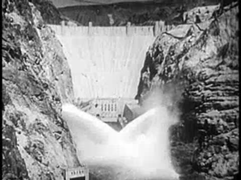 Large concrete dam with massive water discharge gushing from spillways into a river