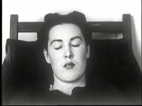 Woman in chair falling into a deeper sleep with her head leaning to one side, static medium shot.