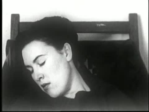Woman's head drooping further to the side as she sleeps deeply in the chair, static medium shot.