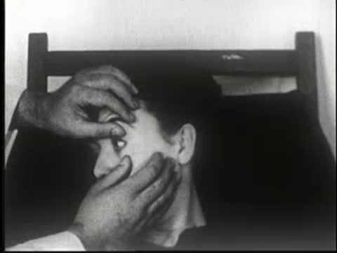 Hands pull open the sleeping woman's eyelids to reveal her eyes, static medium shot.