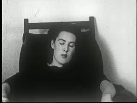 Hypnotized woman sitting in chair with eyes closed, archival medical footage.