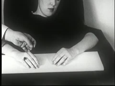 Hypnotized woman at table with hands resting, a hand pricks her finger.