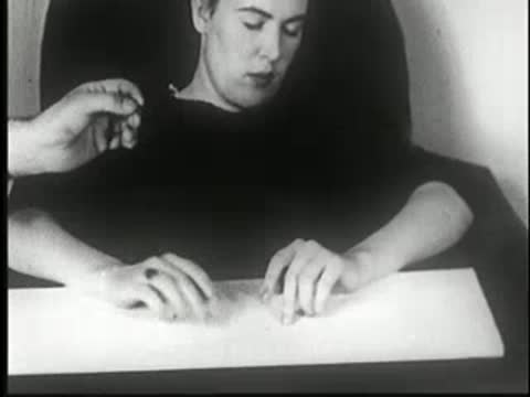 Hypnotized woman at table; a hand touches her right hand.