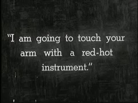 Intertitle on dark background reading: I am going to touch your arm with a red-hot instrument.
