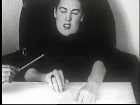 Hypnotized woman reacting in pain as a stick touches her arm at table.