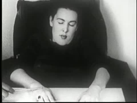 Hypnotized woman resting at table, her expression relaxing after pain suggestion.