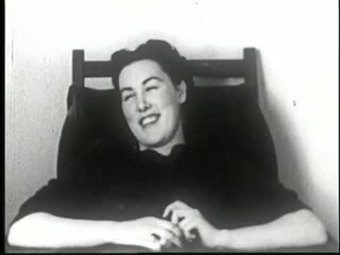A woman sitting upright in a chair with eyes open, looking straight ahead, static medium shot.