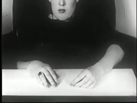 Hypnotized woman sitting at table while someone places a bottle before her.