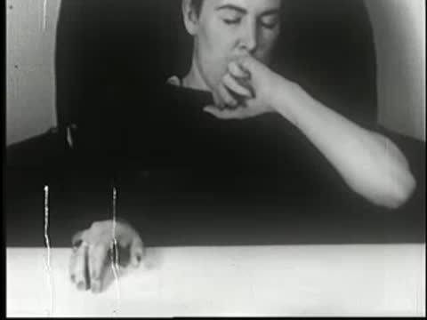 Hypnotized woman grimacing and spitting out liquid after drinking from glass.