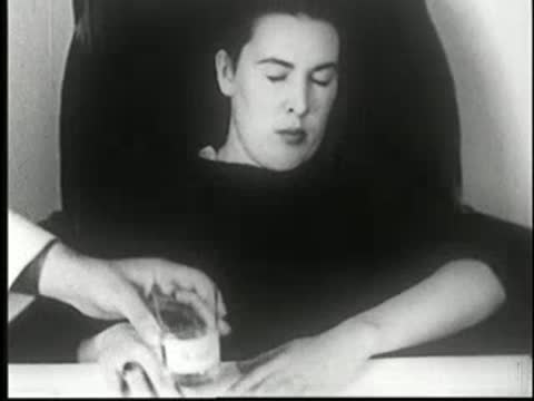 Hypnotized woman sitting at table while a bottle is placed near her hands.