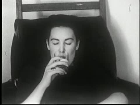 Hypnotized woman calmly drinking from a glass with a neutral expression.