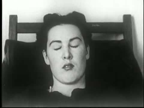 Woman sleeps sitting in a chair in a dark room.