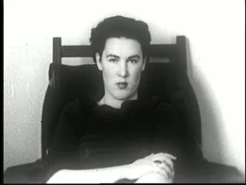 Woman in chair listening to instructions, blinks and shifts slightly, static medium shot.