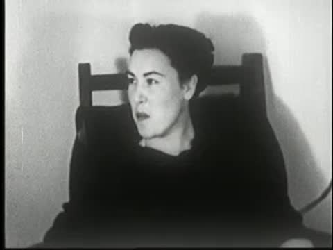 Woman sits in a chair, laughing and looking around.