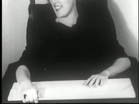 Woman sits at a table and looks down at a blank surface.