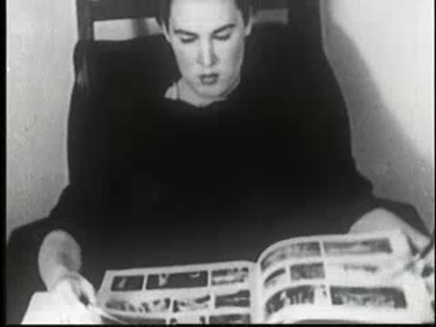 Woman reads a magazine at a table, turning pages.