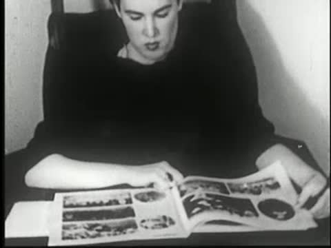 A person smiling while reading a magazine, black-and-white silent era style.