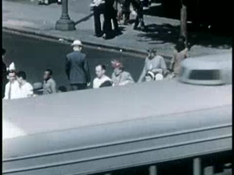 Streetcar moving along a sunny city street lined with pedestrians, 1940s.