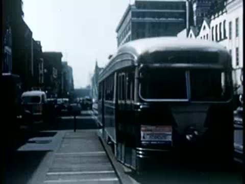 Streetcar traveling down a city boulevard between buildings, mid-20th century.