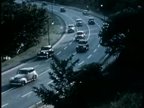 Multiple vintage cars driving along a winding multi-lane highway, 1940s.